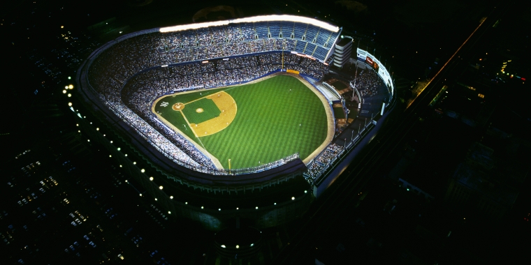 Aerial nighttime view of a brightly lit Yankee Stadium filled with spectators.